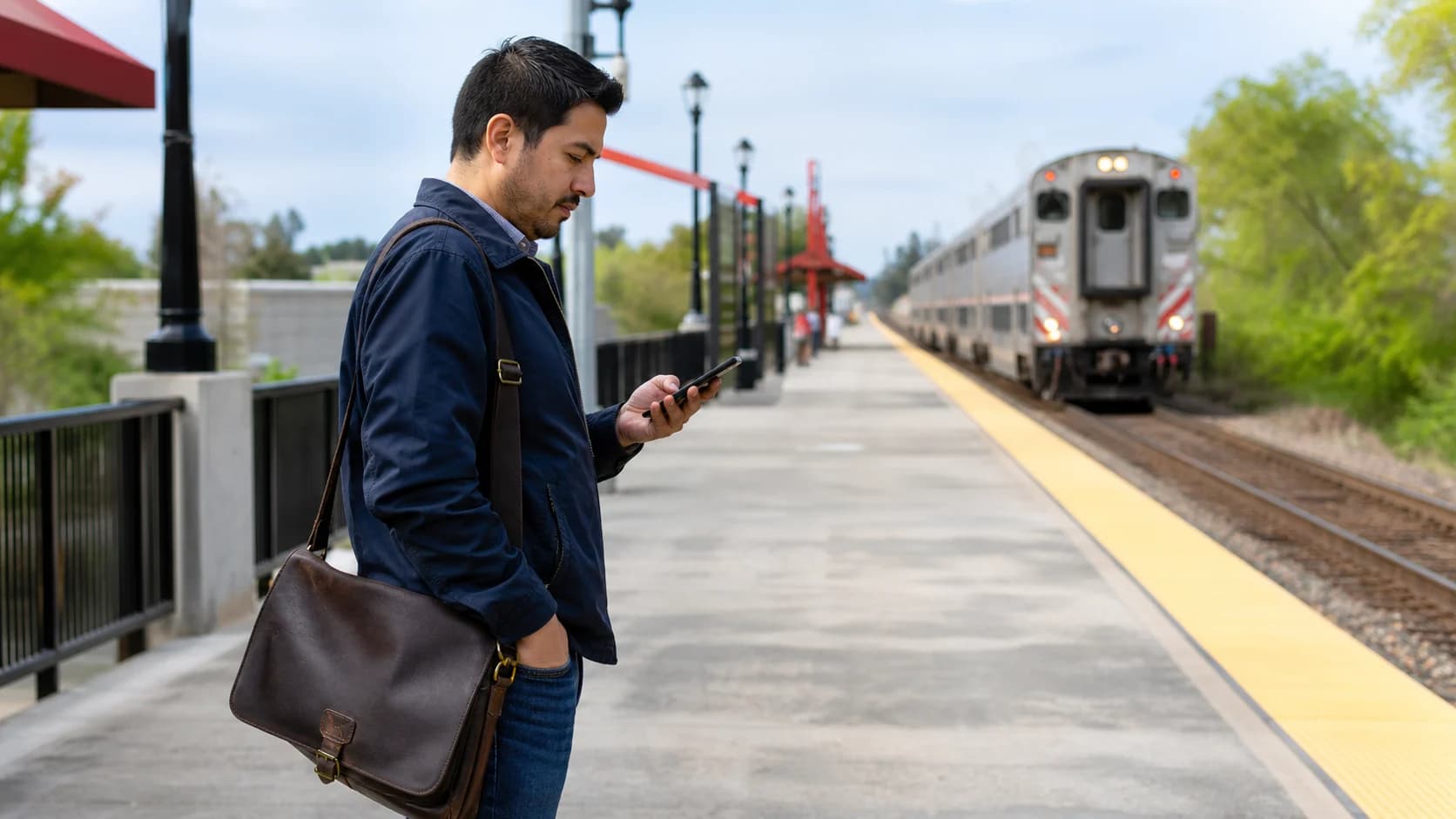 A man checking his phone while standing on a bright commuter rail platform