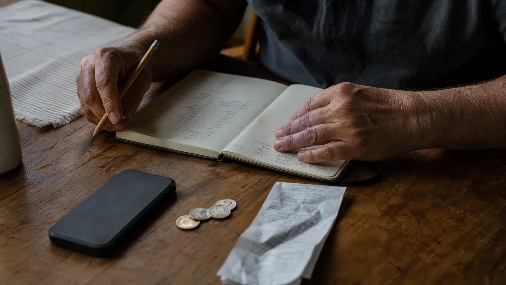A person reviewing a handwritten monthly budget beside a phone and grocery receipt
