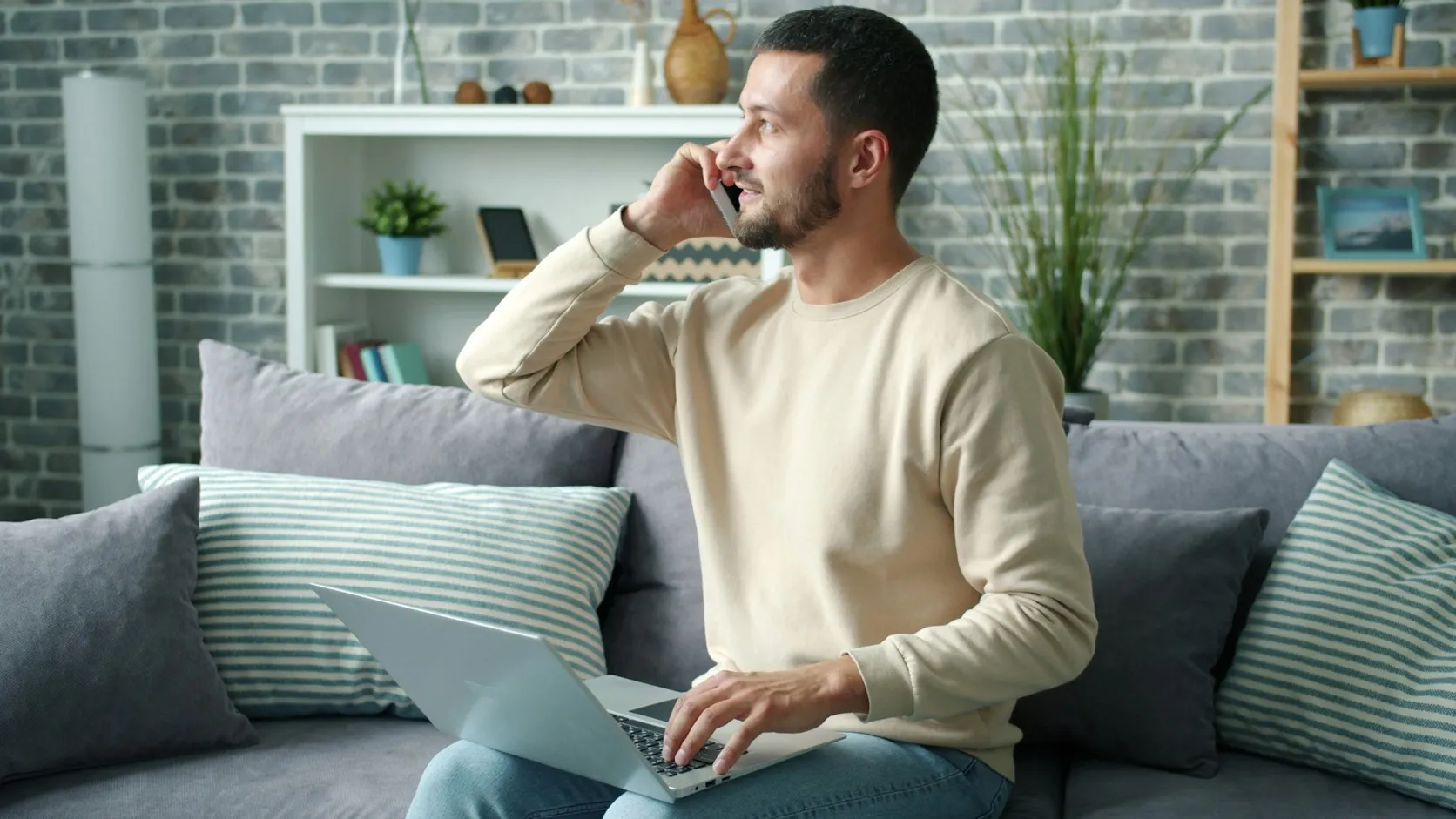 A man on a phone call on his sofa with a laptop on his lap